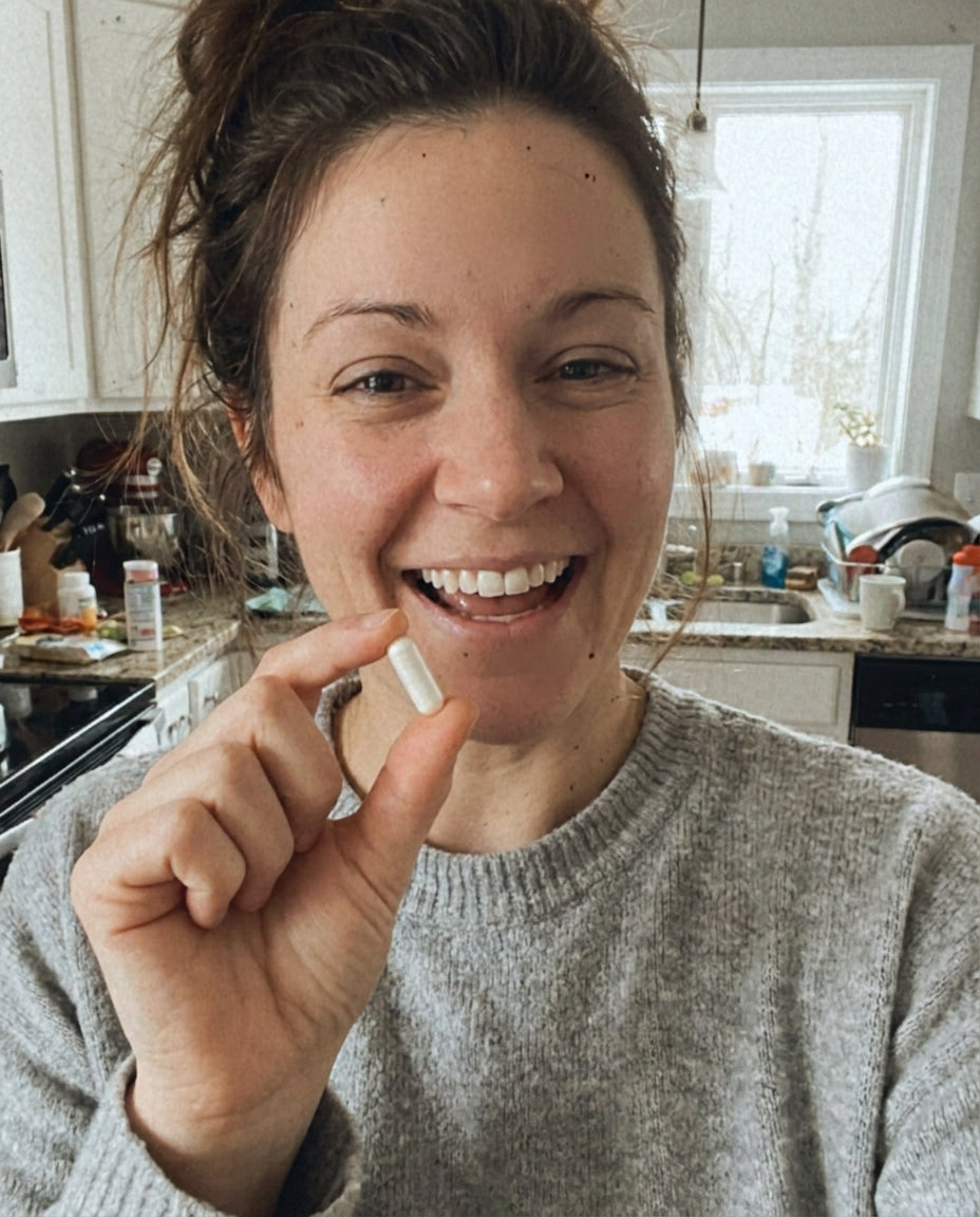 Mom in her kitchen holding a single white LGG probiotic capsule